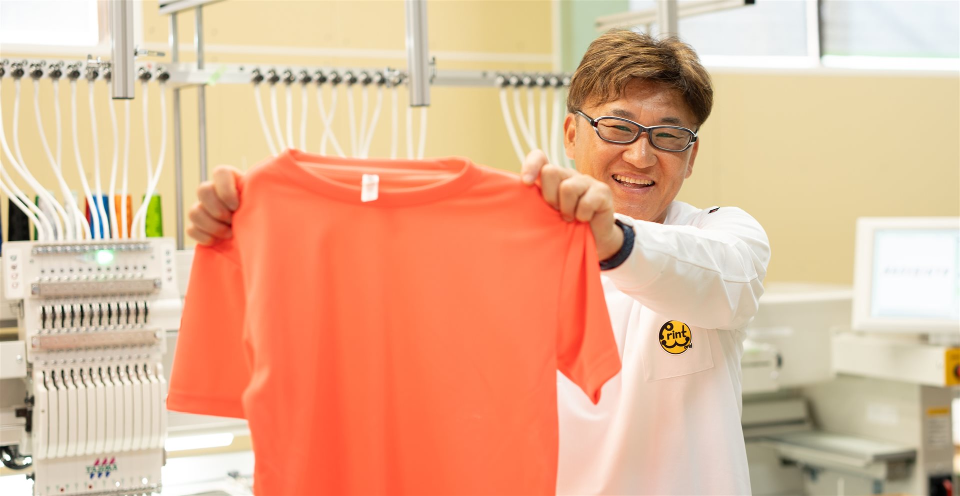 オレンジのTシャツを手に笑顔のスタッフ